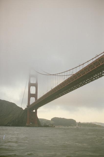 The Golden Gate Bridge viewed from below, the top consumed by a cloud.