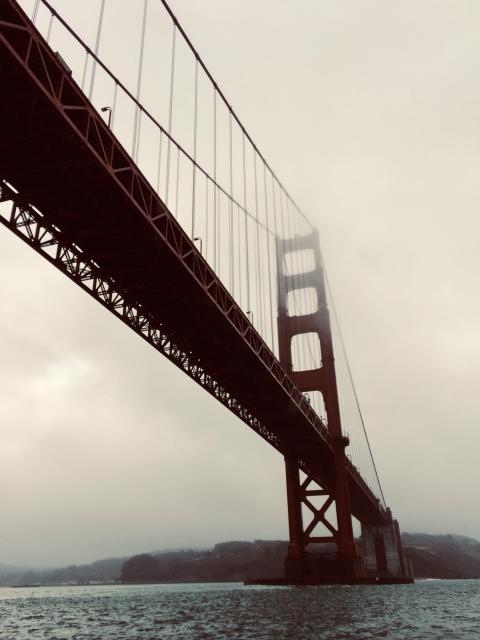 A view of the Golden Gate Bridge on a foggy day with its red structure and suspension cables visible. The bridge spans over a body of water, with hills in the background.