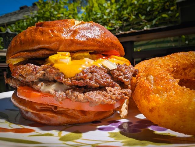 A brightly lit cheeseburger next to a plate of onion rings. The food looks delicious and should make you want a burger.