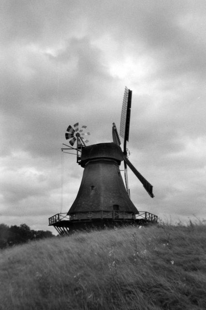 Schwarzweiß-Film-Foto einer Holländermühle vor bewölktem Himmel