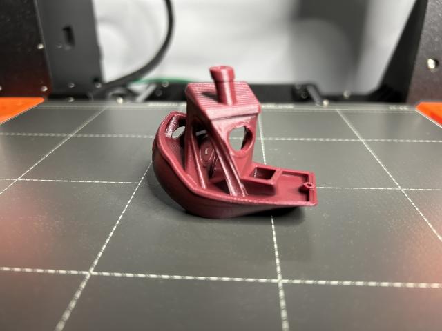 A Benchy printed in merlot red PLA twisted 90 degrees around the Z axis.  It is sitting on the printer bed.