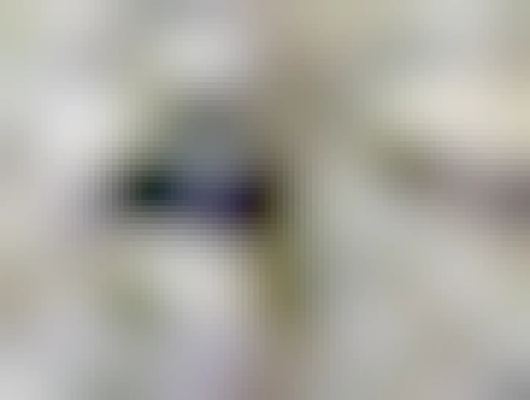 Elliot, black European cat, half under the cover with the left paw coming straight out, miawing at the camera(man) in discontentment, under the white linens of the bed