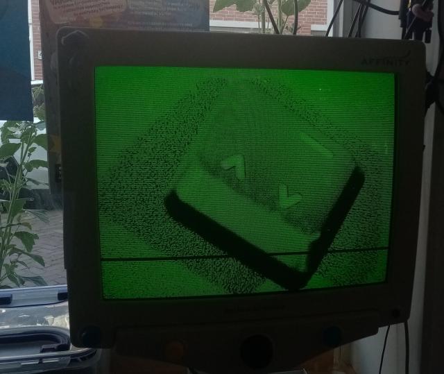 A computer key under a microscope on an old monitor, green coloured. The key is a ^ symbol, both up and down, like two 'v' letters pointing both directions.