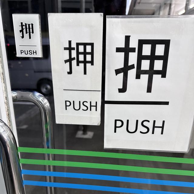 Glass door with three "Push" signs in Japanese and English In increasing size