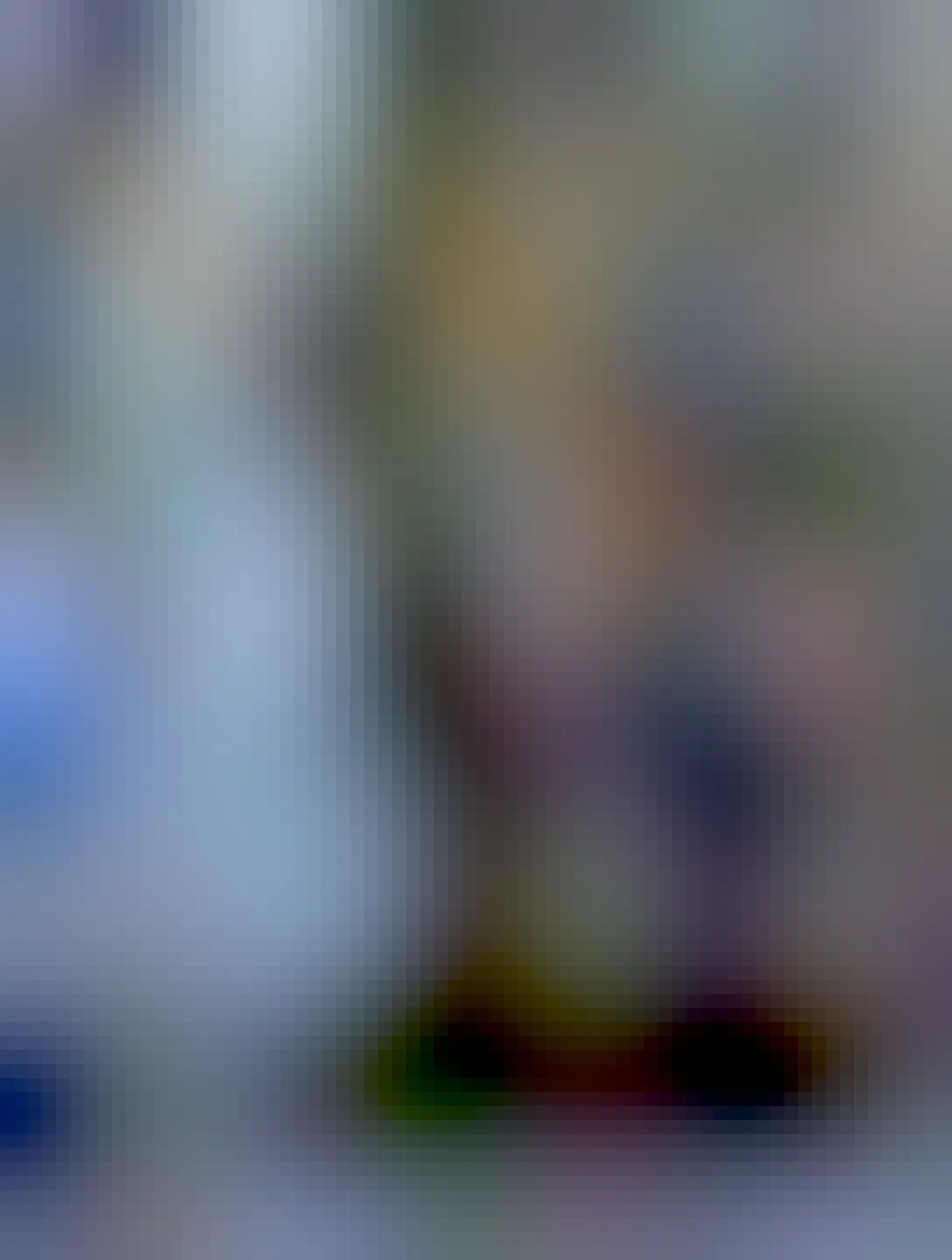 An orange cat sitting upright looking at the camera. He has a white spot on his nose and chest. He has a little collar with a bell on it.The tips of his paws are white.