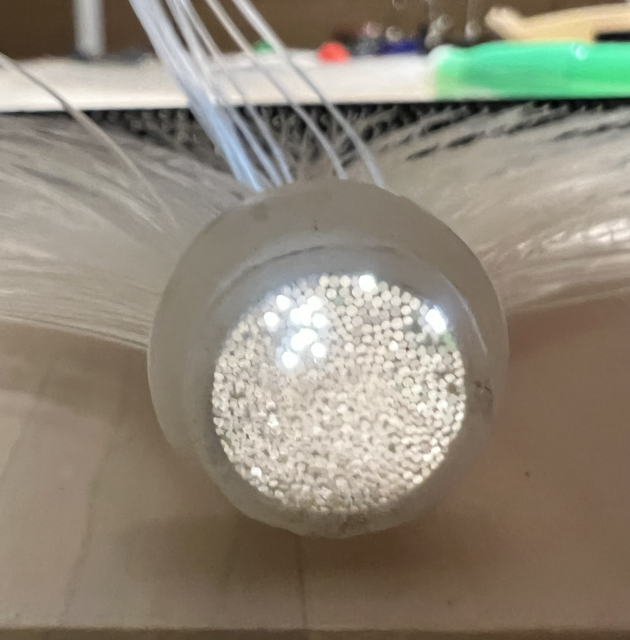 A fuzzy closeup of the business end of 526 cheap plastic fibres. 14 of them are glowing (because I’m shining a torch on the other end). They’re in a cluster with a couple of outliers. 