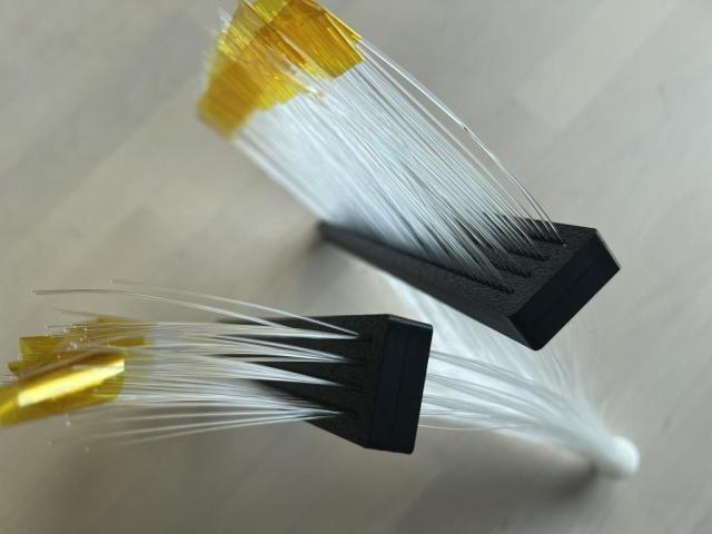A bundle of optical fibres; tightly clustered in a circle at one end, separated into two rectangular grids at the other. The strands are capped off with lengths of yellow tape.