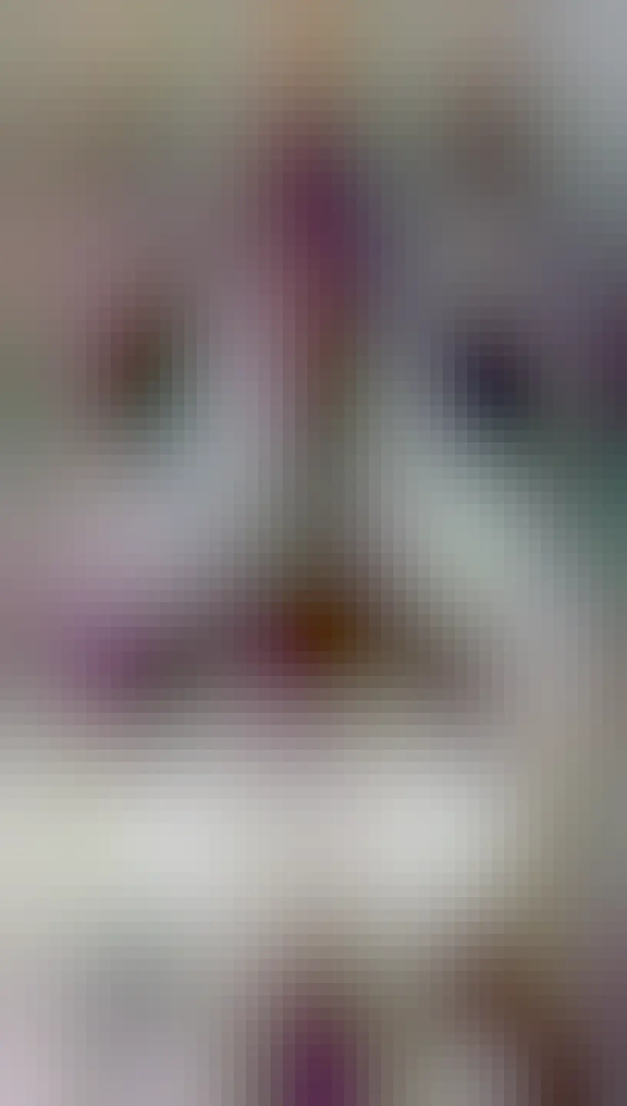 A knitted chicken sits on a sofa apparently looking at the screen of a laptop. 