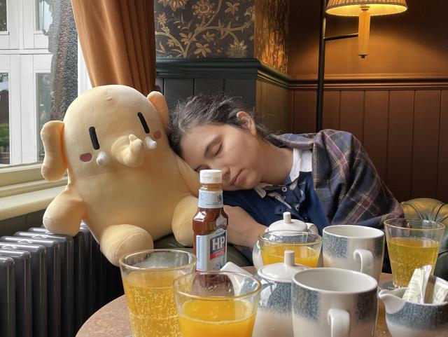 Wife leaning on a large stuffed Mastodon toy with her eyes closed, in front of a table with tea pots and tea mugs. 
