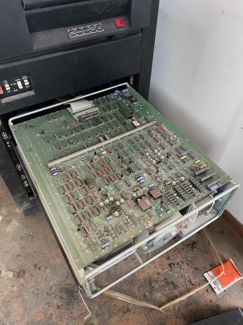 Photograph of one of the compute module trays pulled out of the lower part of the computer. It is a large circuit board with a ribbon cable trailing off the back into the computer.