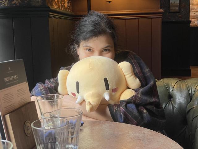 Wife squishing a stuffed Mastodon toy in an embrace in front of a table. 