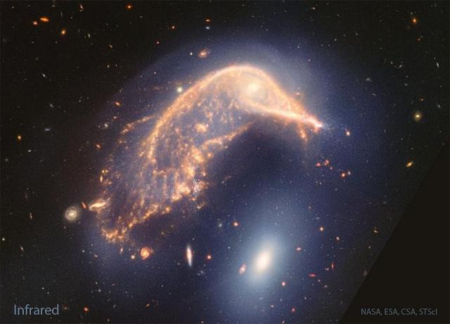 Two large interacting galaxies are shown. The upper galaxy, has significant internal structure and is curved over the lower galaxy which is a featureless oval.