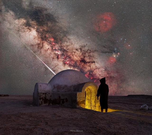 A starry sky is seen above a structure with an iconic dome. A person in shadow stands at the entrance. Sloping down in the sky is the central band of our Milky Way Galaxy. Just below the Milky Way is the streak of a bright meteor.