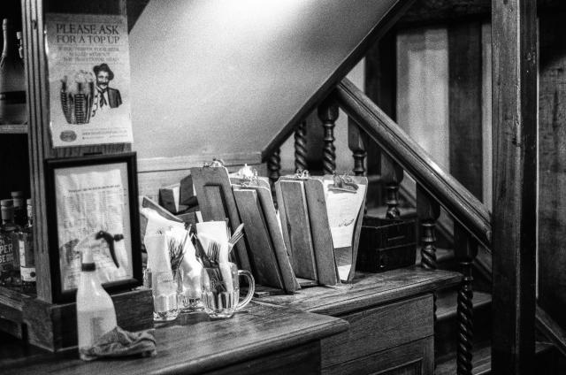 Clipboards, glass mugs filled with cutlery and serviettes, a spray bottle of cleaning fluid, posters on the wall, all underneath a staircase.