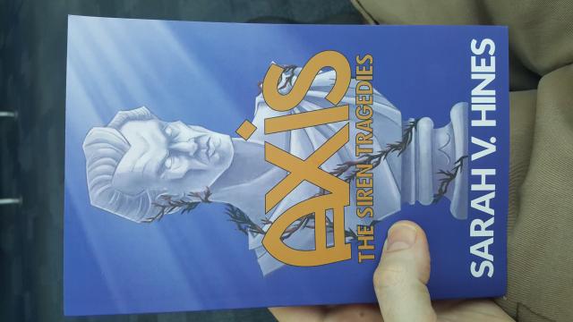 Me, holding the book Axis, by Sarah V. Hines, over my lap.