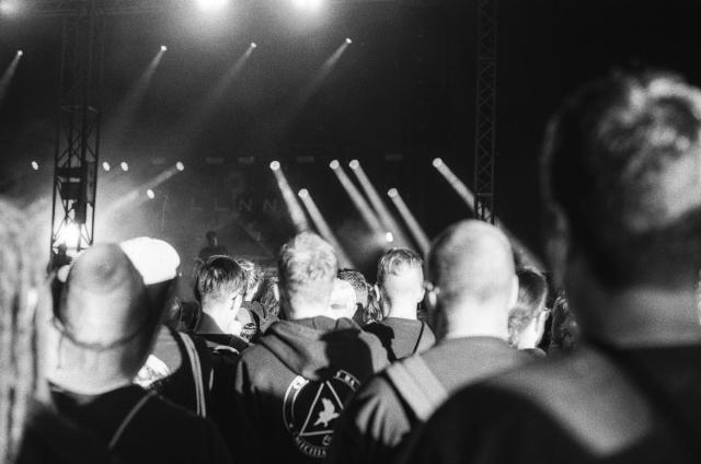 A crowd, facing away, illuminated by evening sunlight, while the stage in the distance is dark with clearly defined stage lights.