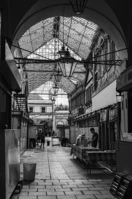 A street covered by a triangular glass roof, street lamps suspended in the middle.