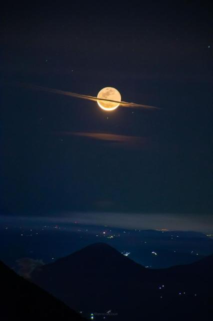 The featured image shows a crescent Moon over a city and volcano with a flat cloud running through the center that makes the Moon look a bit like the planet Saturn.