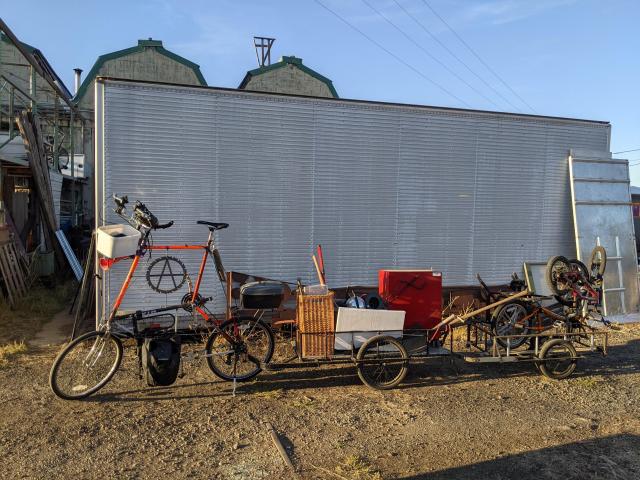 Picture of an orange tall bike that is parked with two trailers attached to it 