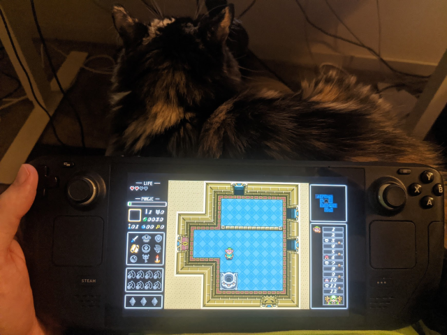 Steam Deck playing a fan made game of Legend of Zelda: Dungeons of Infinity with a friendly cat in lap.