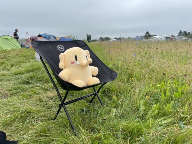 The stuffed Mastodon toy sitting in a camping chair in a green field.