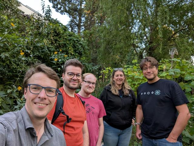 Josh, Thibault, Travis, Amandine, and Matthew stand together for a group selfie in front of a lush garden.