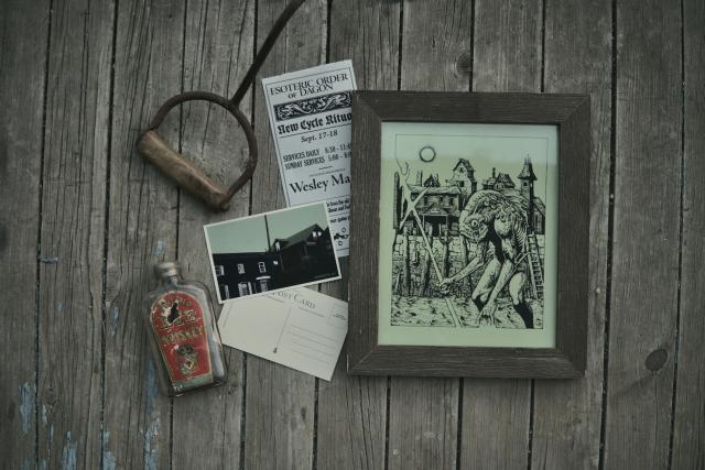 a green-tinted print of a deep one in front of a fishing town with a pamphlet from the esoteric order of dagon and a postcard of innsmouth