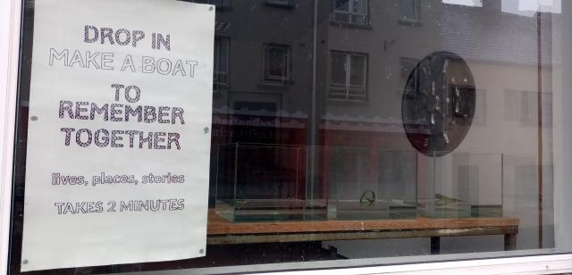 A sign for an event making boats in a window, with three water tanks just visible.