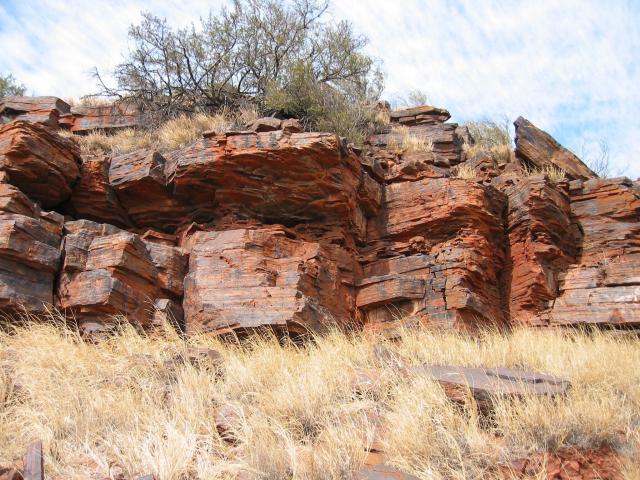 photo of an outcrop of rusty red rocks in a drey grassy landscape 