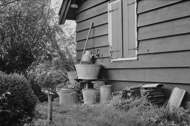 A pile of buckets and jugs, and a pile of unused roof tiles behind a shed