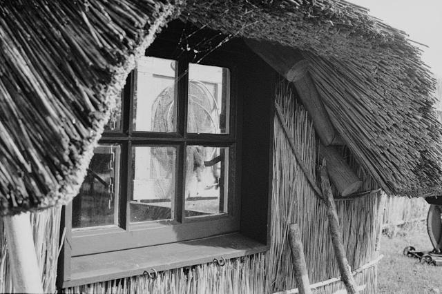 Looking through the window of a thatch-roofed shed, where fishing nets are hung