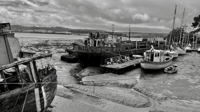 A small todal harbour — at low water, nothing but mud — its breakwaters formed by rusted commercial hulks. Yachts lie with their keels in the mud against an rickety timber pontoon.