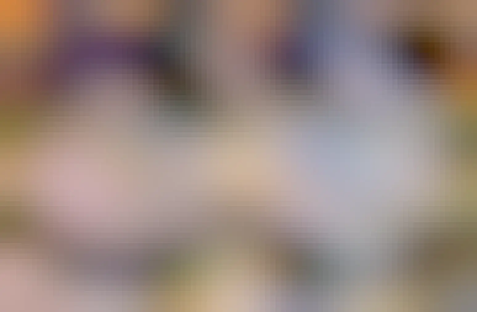 Two photos of a very cute and fluffy tuxedo cat with two black spots that looks like a tiny mustache. The first picture of the kitty is looking down some and, in the second one, looking at the camera while giving a tiny blep 👅