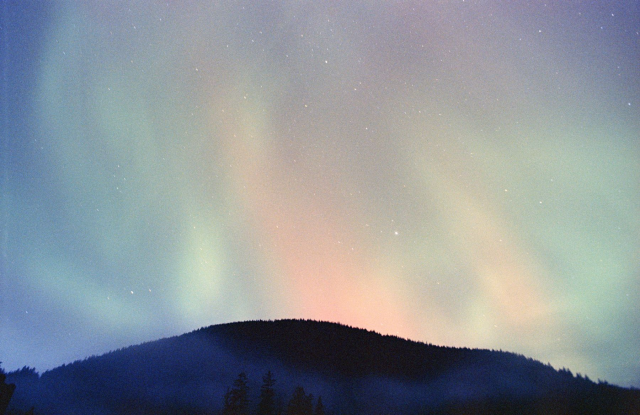 multicolor aurora over a hill with fog covering the tree tops
