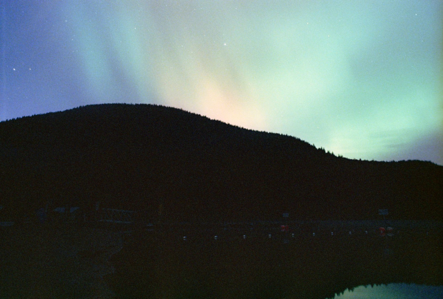 multicolor aurora over a hill and a tiny slice of water that reflects it