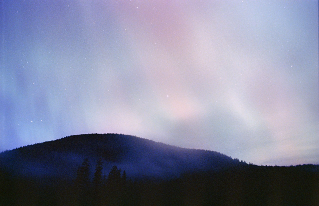 a large multicolor aurora display over the hill with fog rolling over the hill