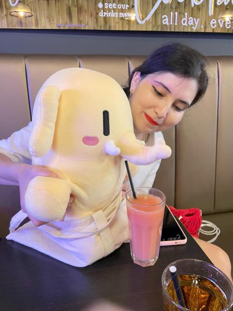 Mastodon stuffed toy having a sip of guava juice at a cafe.