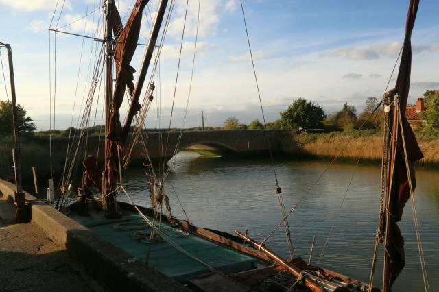 A riverside quay, by a bridge, with a moored, vintage yacht.