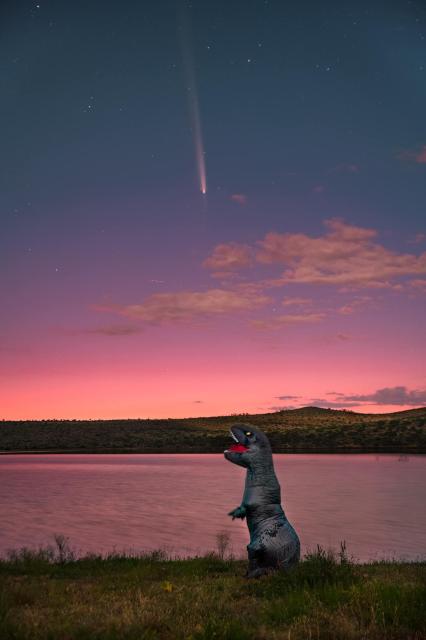 Photo (no text) by Daniel Koronado 

Comet in sky streaks towards horizon 
A “dinosaur” (prop) looks up from the edge of a lake .