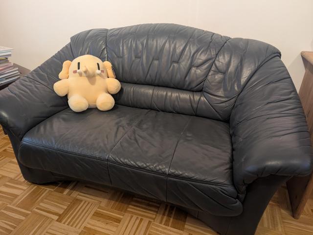 A yellow plush elephant sitting on the left side of a dark blue leather couch