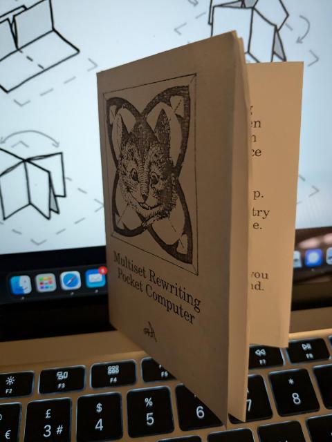 A folded paper with a cat and the text "Multiset Rewriting Pocket Computer"