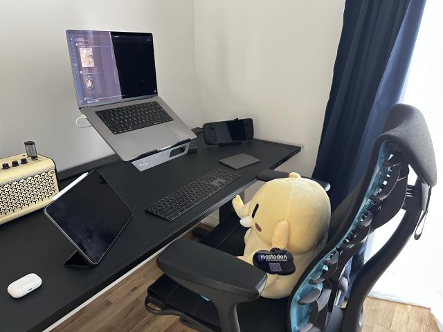 A photo of a home office setup with Mastodon plushie sitting in the chair 