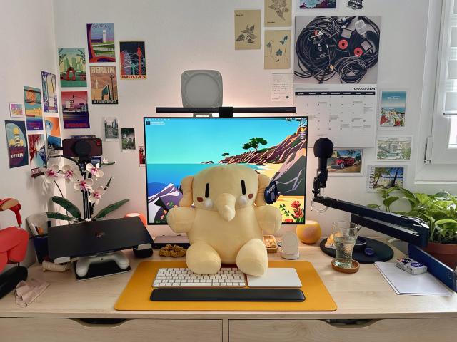 Plushtodon, the official Mastodon plushie, sitting on my desk right in front of my monitor