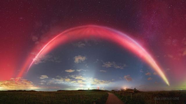 A night sky is shown with a bright red band running overhead. Above the red band is a diffuse red glow. A path through a grassy filed is in the foreground with a path going out toward the horizon.