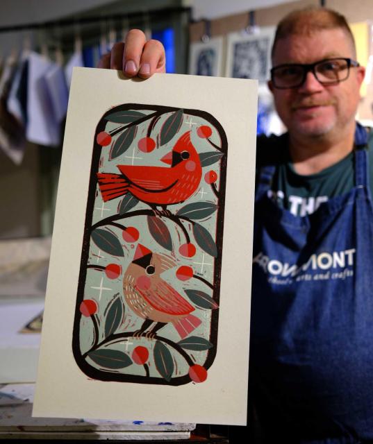 photo of artist, ken swinson holding a beautiful woodcut that features two cardinals: a bright red male and pale brown female. they are perched in branches with cherries or berries.