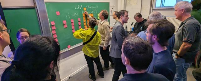 Attendees of the fosdem EU Policy DevRoom workshop ideas for implementation of the Cyber Resilience Act in front of a chalk board and post-it notes.