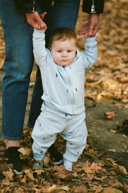 An infant standing with help from an adult.