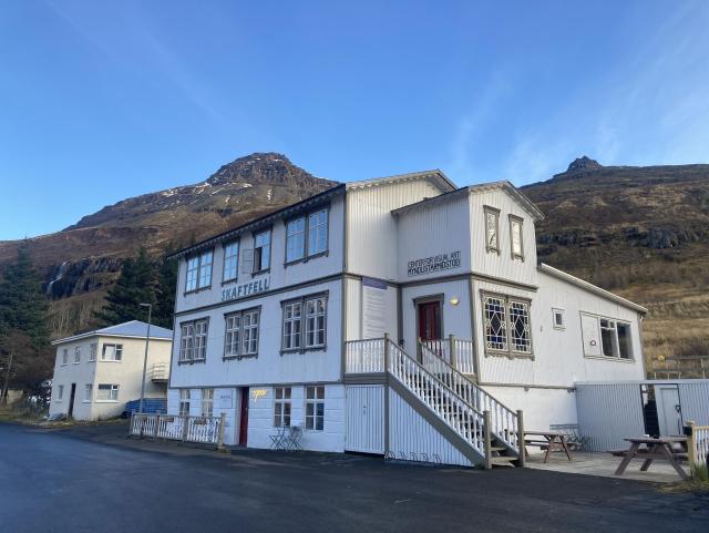 A photo of the Skaftfell art Center, which is a white wooden house at the foot of a mountain in Seydisfjordur in Iceland. 
