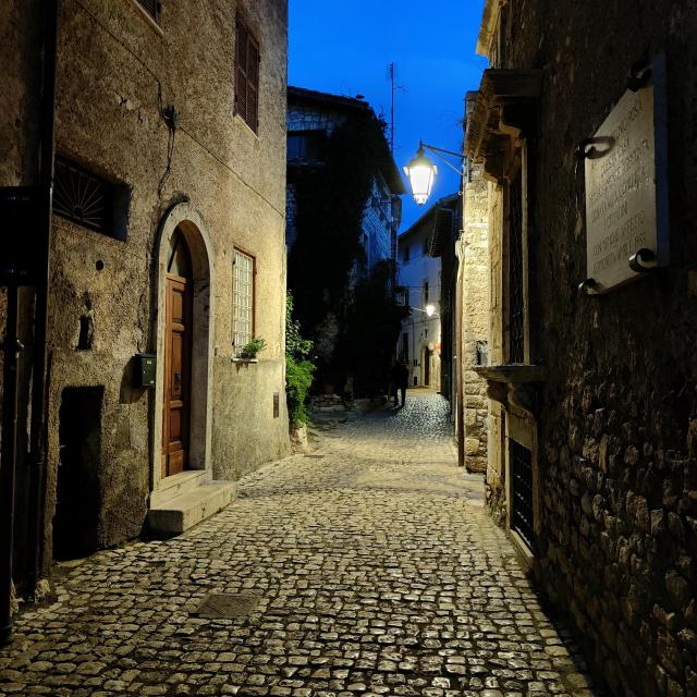 A street paved with sampietrini, lit by a suspended lamp. It's almost night.