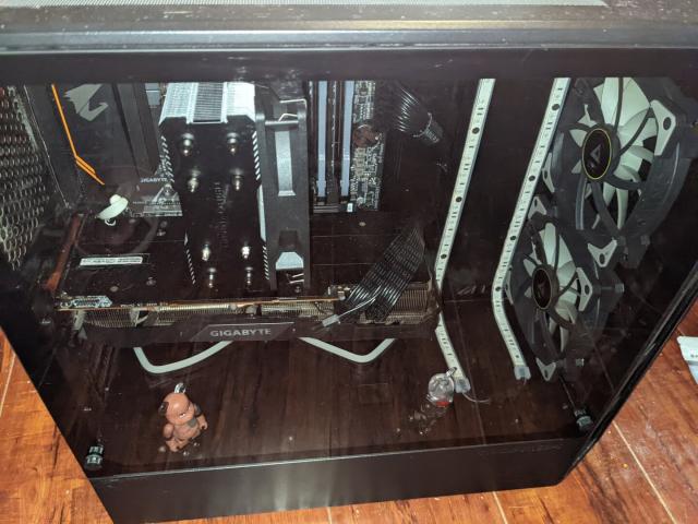 Photo of a desktop PC in a bedroom. PC is black with a glass panel to reveal the components inside